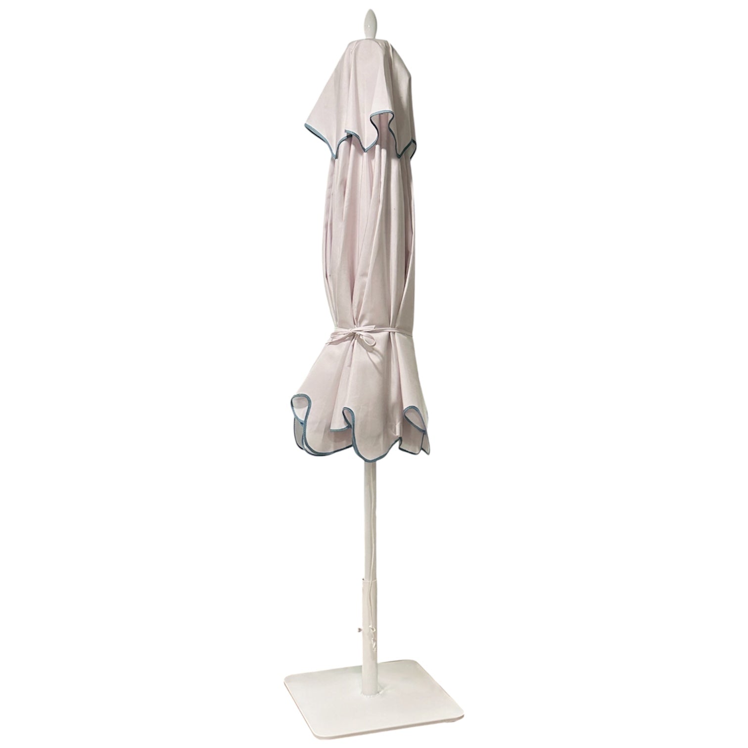 The Montecito Hex Umbrella by Santa Barbara Umbrella is a closed white patio umbrella with blue trim, tied at the middle and standing upright on a square base—perfect for adding elegance to any stylish outdoor space.