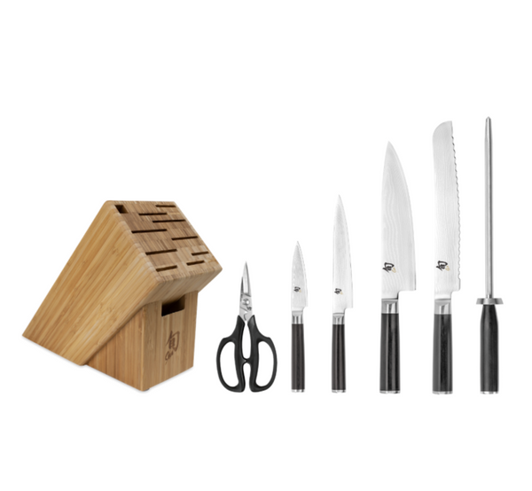 The Shun Classic Ebony Essential 7-Piece Knife Block Set elegantly displays four expertly crafted knives, kitchen shears, and a honing steel in a neat row on a white background.