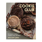 A marble tray holds chocolate cookies and a glass mug of hot chocolate. The book “Cookie Club” by Penguin Random House is featured, hinting at irresistible cookie recipes from this popular cookbook.