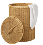 The Pigeon & Poodle Morris Hamper is a round, hand-woven basket with a matching lid resting nearby and a white towel draped over its rim.