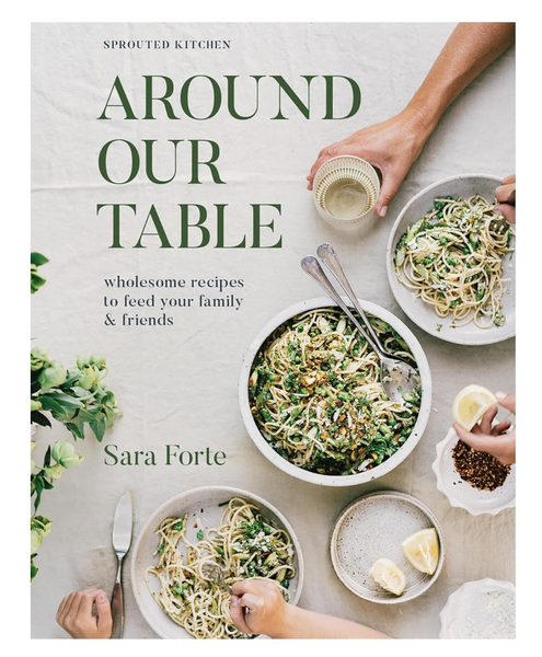 The cover of "Around Our Table: Wholesome Recipes to Feed Your Family and Friends," a cookbook by Sara Forte and published by Chronicle Books, highlights nourishing recipes from Sprouted Kitchen, including pasta dishes with greens and a hand reaching for a glass of white wine.