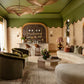 Elegant living room with green walls, plush furniture, and a stylish bar area, accented by the unique Indonesian Bamboo Chandelier from Balsamo Antiques and arched doorways at the Kips Bay Show House.