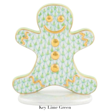 The Herend Gingerbread Man Collection features a porcelain gingerbread-shaped figure with hand-painted green and gold patterns, gold buttons, and accents on a white base. "Key Lime Green" appears below for a touch of artistic flair.