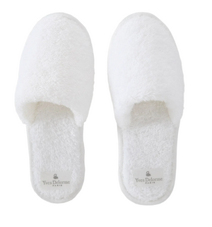The Etoile Blanc Slippers by Yves Delorme are white, closed-toe terry cloth slippers made from long-staple cotton for absorbency, with "Yves Delorme Paris" inscribed on the insoles.