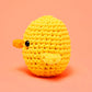 Kiki the Chick Beginner Crochet Kit by The Woobles is a round, yellow, crocheted stuffed toy—ideal for beginner crochet projects—featuring a small black eye and two side flippers, shown against a solid peach background.