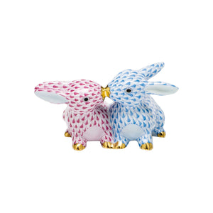 Herend’s Kissing Bunnies are two hand-painted porcelain rabbit figurines, one pink and one blue, with gold-tipped noses touching and a signature scale-pattern design.