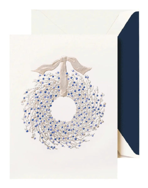 The Crane Juniper Berry Wreath Card Set features an intricately engraved design showcasing a wreath of juniper berries in blue and white, accented with a ribbon on a minimalist background, ideal for sending holiday greetings.