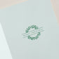 The Twinkling Palms Card Set by Crane features a white card adorned with a green wreath of Fraser Fir sprigs and "Merry Christmas" printed at the center.