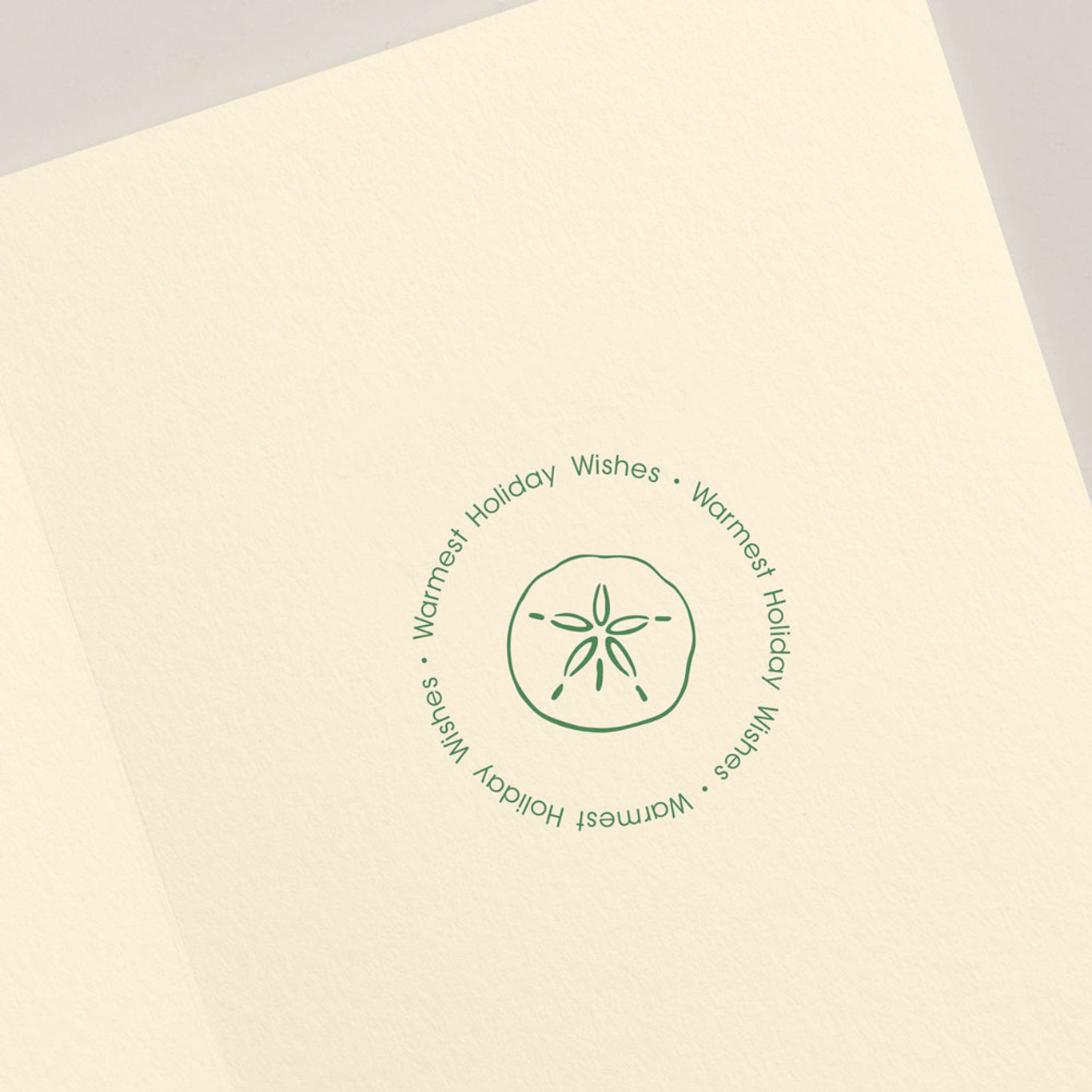 The Crane Seashells Wreath Card Set by Crane showcases a sand dollar illustration with a coastal vibe, accompanied by the elegantly repeated text "Warmest Holiday Wishes" in a circular pattern.