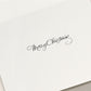 The Skating Noel Holiday Card Set by Crane features elegant black cursive "Merry Christmas" lettering on a white card, perfect for spreading festive cheer.
