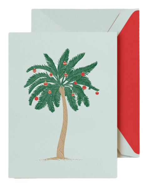 The Crane Trimmed Palm Tree Card Set by Crane showcases a card with a palm tree decorated with red ornaments on the front. A red-lined envelope peeks from behind, enhancing its festive appeal.