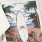The Engraved Coastal Holiday Card Set by Crane features a surfboard with a red bow, gift boxes, palm trees, and a hut on the beach—ideal for sending seaside holiday cheer.