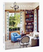The book Romancing the Home by Rizzoli features a cover with a living room accented by blue chairs, shelving, and a large window—an ideal display of classic-meets-modern bespoke interiors.