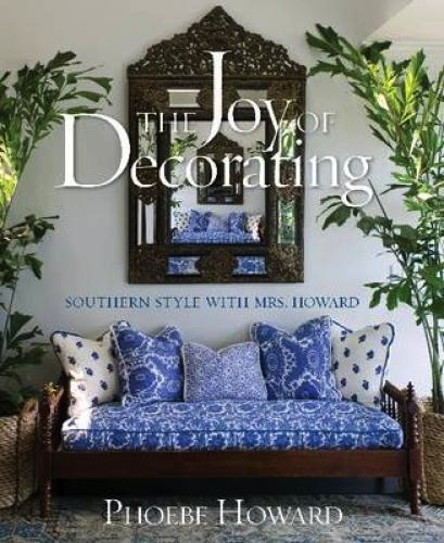 A decorative book cover with a patterned sofa, large plants, and a mirror captures luxury. Titled "Joy of Decorating by Phoebe Howard," the subtitle says "Southern Style with Mrs. Howard," published by Abrams.