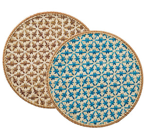 The Lanai Placemat Collection by Kim Seybert features two round rattan placemats with a star pattern—one in brown, one in blue and beige—both finished with natural fiber borders for added style.