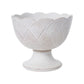 The Le Panier Mystic Knot Collection by Juliska features a white ceramic pedestal bowl with a scalloped rim and textured, geometric pattern inspired by French basket weave.