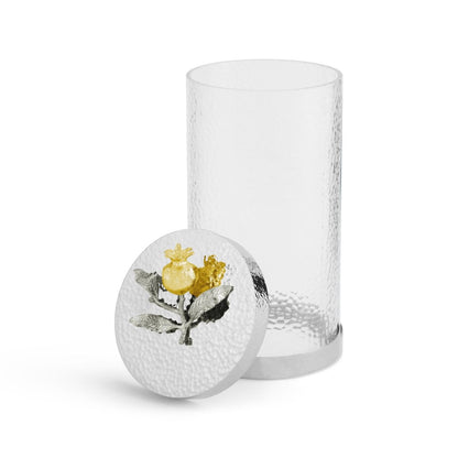 A clear, textured glass canister with a white lid—decorated with a painted lemon and leaves—evokes the elegant artistry of Michael Aram’s Pomegranate Silver & Gold Canister. Shown with the lid off and resting against the container.