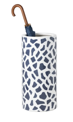 A blue umbrella with a wooden handle stands in the Pigeon & Poodle Yuba Umbrella Stand, which features a white cylindrical shape and a navy irregular geometric, hand-applied print.