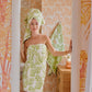 A woman stands in the bathroom doorway, wrapped in a green floral towel from the Weezie Towels x Meg Braff Bath Collection. A matching towel hangs on the wall against Palm Beach-inspired wallpaper, reflecting the elegant style of Meg Braff and Weezie Towels.