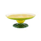 The Lemon Collection cake stand by Bordallo Pinheiro is a whimsical ceramic piece with a lemon slice design on top, yellow sides, and a green leaf-textured base.