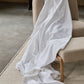 A Bovi White Finnley Blanket, made from 100% cotton, is draped over a beige upholstered chair and onto a light rug on a concrete floor—adding an inviting hint of premium European style.