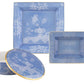 Three blue porcelain pieces from the Ginori 1735 Oriente Italiano Pervinca Collection—two square plates and a round lidded container with white floral designs and gold trim—are displayed against a white background.