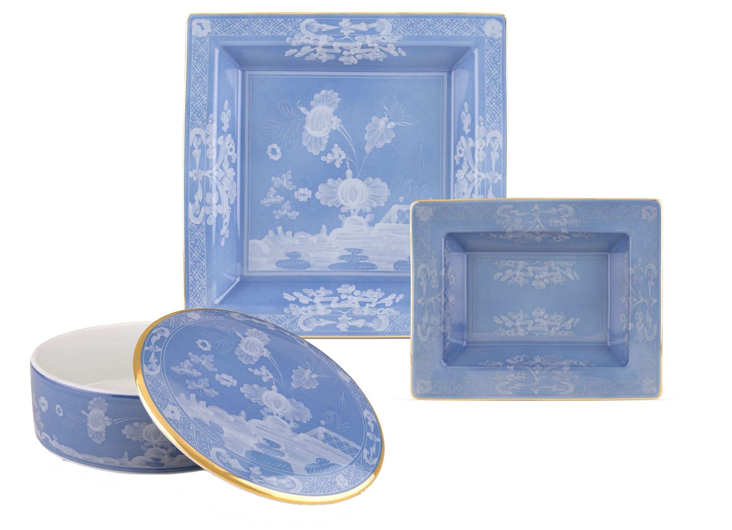 Three blue porcelain pieces from the Ginori 1735 Oriente Italiano Pervinca Collection—two square plates and a round lidded container with white floral designs and gold trim—are displayed against a white background.