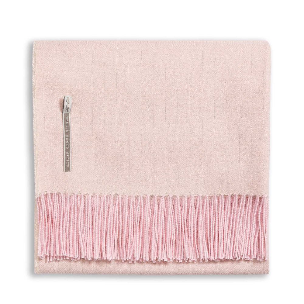 Alicia Adams Alpaca's Classic Herringbone Throw Collection features a folded, light pink alpaca blanket with fringe edges and a small fabric label, all fair trade made in Peru.
