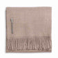Alicia Adams Alpaca's Classic Throw, a folded beige blanket from the Alicia Adams Alpaca collection, is crafted from cashmere and baby alpaca, featuring fringes on the bottom edge and a small fabric tag on the left side. It is fair-trade made in Peru.