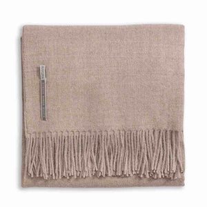 Alicia Adams Alpaca's Classic Throw, a folded beige blanket from the Alicia Adams Alpaca collection, is crafted from cashmere and baby alpaca, featuring fringes on the bottom edge and a small fabric tag on the left side. It is fair-trade made in Peru.