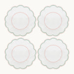 Four white, round, scalloped-edge plates with pink and green borders are arranged in a 2x2 grid, shown alongside the Duggan Society’s Lilibeth Table Linen Collection—perfect for your next gathering.
