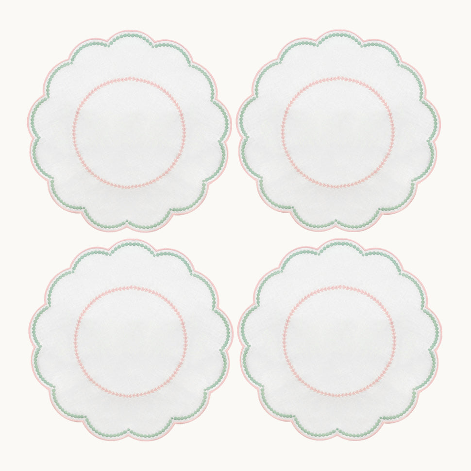Four white, round, scalloped-edge plates with pink and green borders are arranged in a 2x2 grid, shown alongside the Duggan Society’s Lilibeth Table Linen Collection—perfect for your next gathering.
