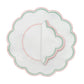 The Duggan Society Lilibeth Table Linen Collection features a round white scalloped embroidered placemat with green dots and pink trim, topped with a matching folded linen napkin—perfect for stylish table settings.