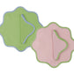 The Duggan Society Daisy Table Linen Collection features two elegant scalloped-edge placemats—green with blue trim and pink with green trim—each paired with a hand-dyed linen napkin for a refined setting.