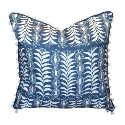 The Little Zanzibar Down Pillow by Hive Custom Pillows features a square blue 22x22 design with white botanical patterns and small white pom-poms along the edges, displayed against a white background. This handmade pillow is perfect for adding a charming touch to any room.