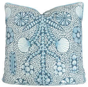 The Shell Grotto Seaside Outdoor Pillow by Associated Design features blue and white geometric and floral patterns, expertly crafted for durability and style, making it a standout accent against any crisp white background.
