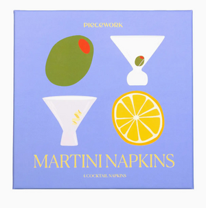 A lavender box adorned with illustrations of martini glasses, an olive, and a lemon slice showcases the elegant Cocktail Napkin Collection by Piecework. The packaging reads “PIECEWORK COCKTAIL NAPKIN COLLECTION 4 COCKTAIL NAPKINS,” making it an ideal choice for anyone seeking stylish and sophisticated cocktail napkin sets.