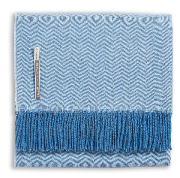 The Alicia Adams Alpaca Classic Throw in Sky Blue is a baby alpaca herringbone throw with fringed edges and a small tag, showcasing timeless elegance.