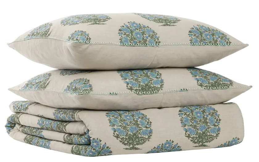 A pair of beige pillows and a folded quilt from the John Robshaw Vani Leaf King Duvet Set, all adorned with a blue and green floral pattern inspired by Rajasthan palace bedding, displayed against a white background.