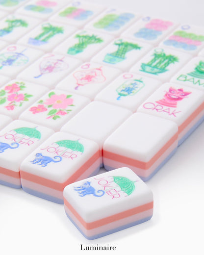 The Oh My Mahjong Mahjong Tile Collection features stylish pastel tiles with floral, animal, and plant designs, neatly arranged with one hand-painted tile displayed in the foreground.