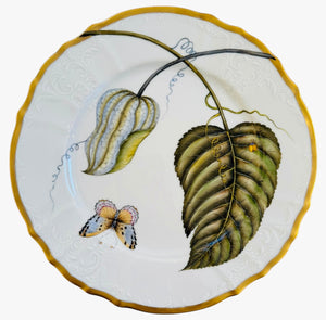 The Anna Weatherley Elegant Foliage Dinner Plate Collection features hand-painted porcelain with a gold rim, textured vine, butterfly, and two green leaves for an elegant decorative accent.