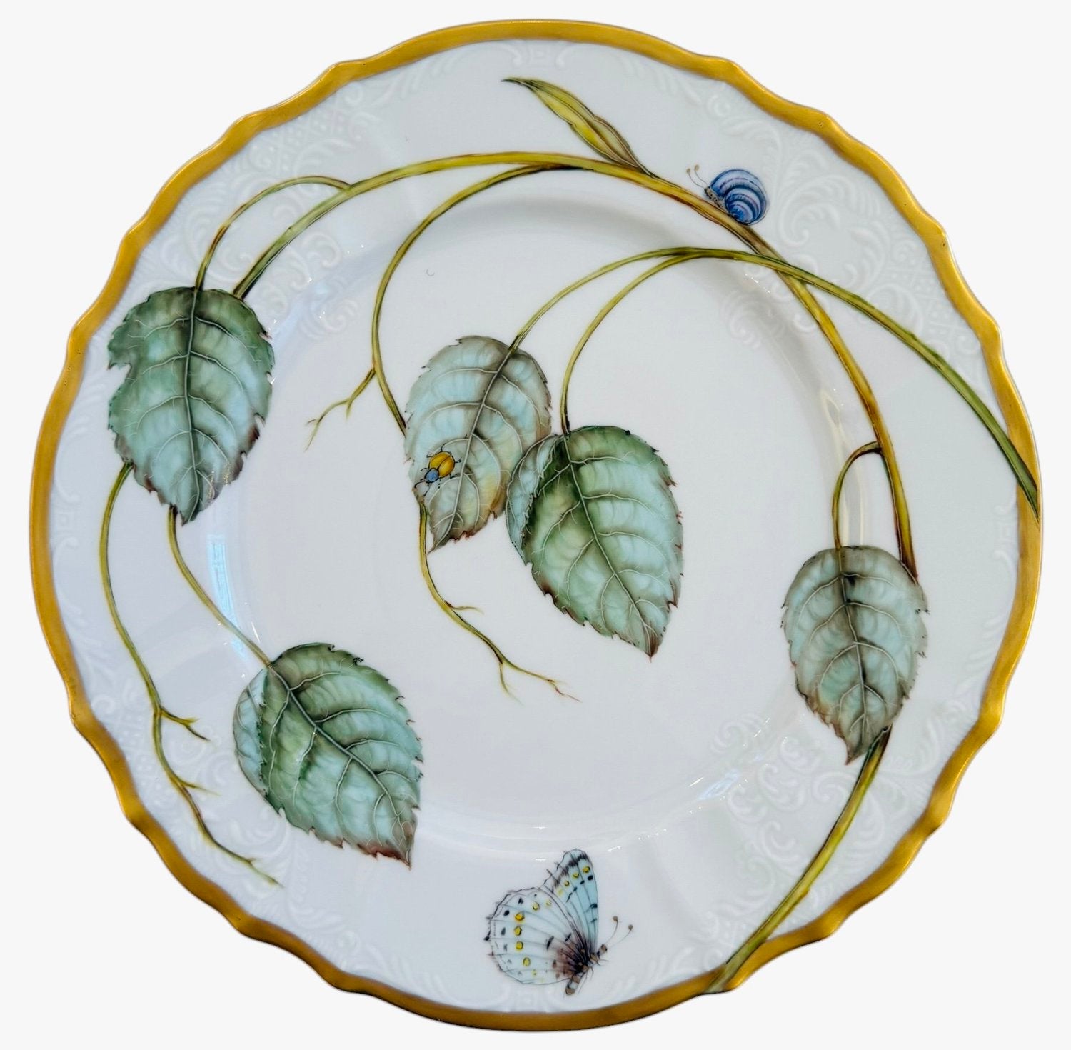 The Elegant Foilage Dinner Plate Collection by Anna Weatherley features hand-painted green leaves, a blue snail, and a butterfly on white porcelain with gold trim—a stunning limited edition for collectors.