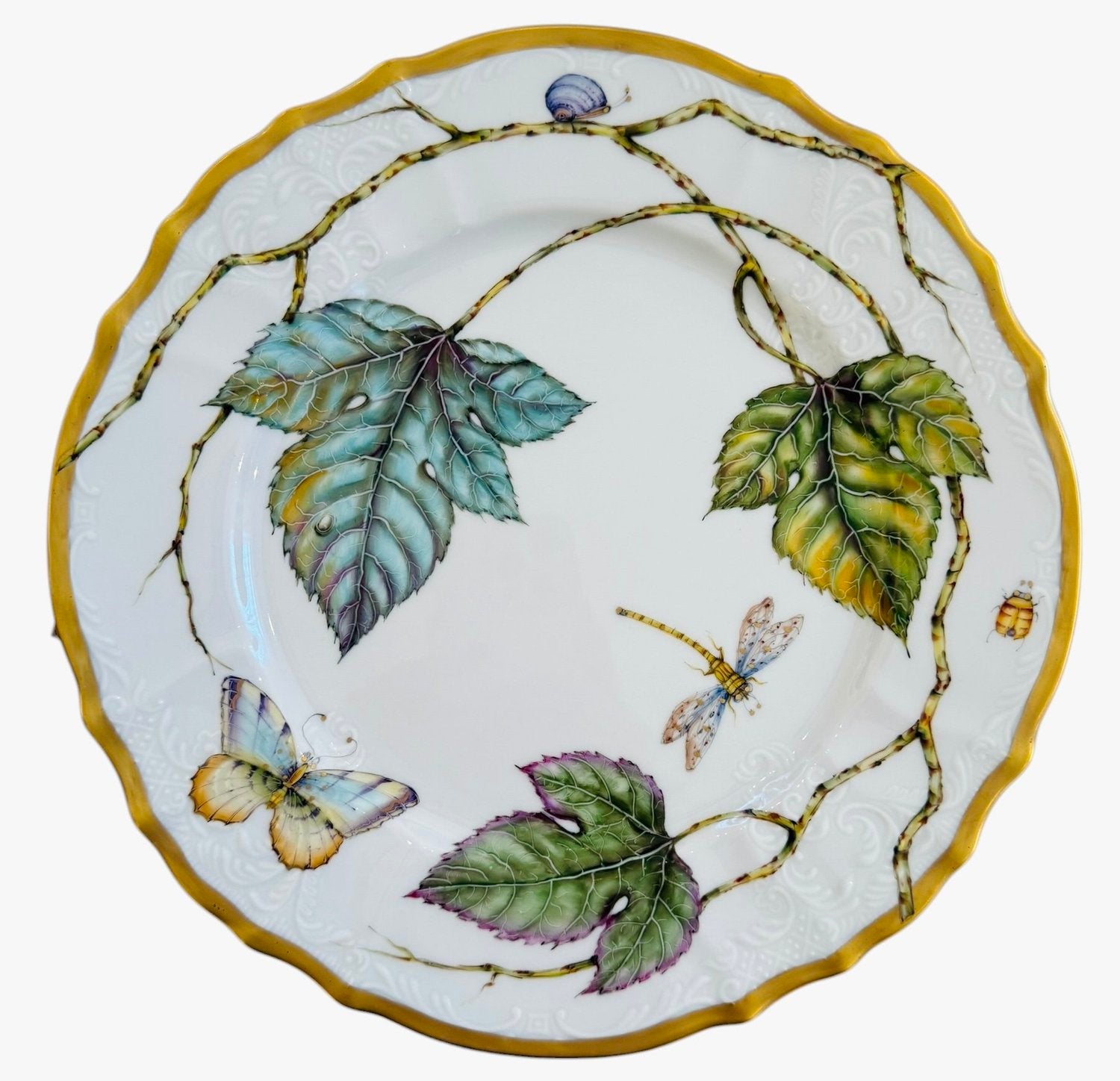 The Elegant Foliage Dinner Plate Collection by Anna Weatherley features hand-painted porcelain plates with scalloped yellow trim, adorned with leaves, a butterfly, a dragonfly, a bee, and a snail in her signature style.