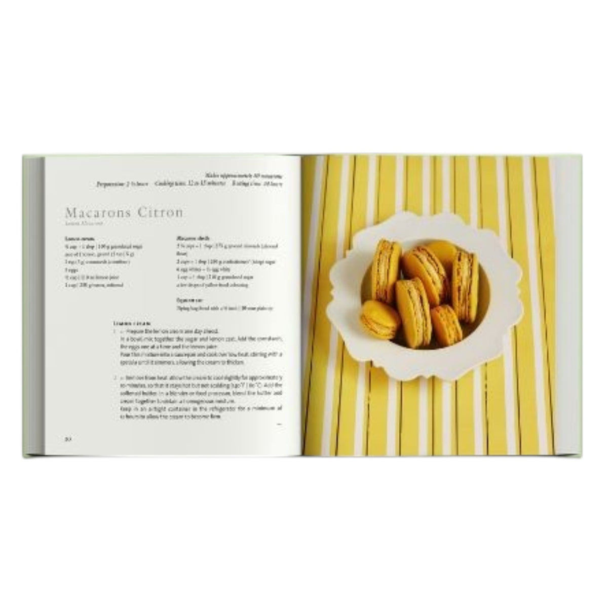 An open Simon & Schuster Ladurée Macarons cookbook displays a recipe on the left, while a plate of yellow Ladurée macarons sits on the right, all arranged on a yellow-striped surface.