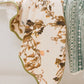 Two towels hang side by side: a luxury bath towel with a green and white geometric pattern, and the Vivian Magnolia Floral Scallop Bath Towel by Weezie Towels, featuring a brown and green floral design on white.