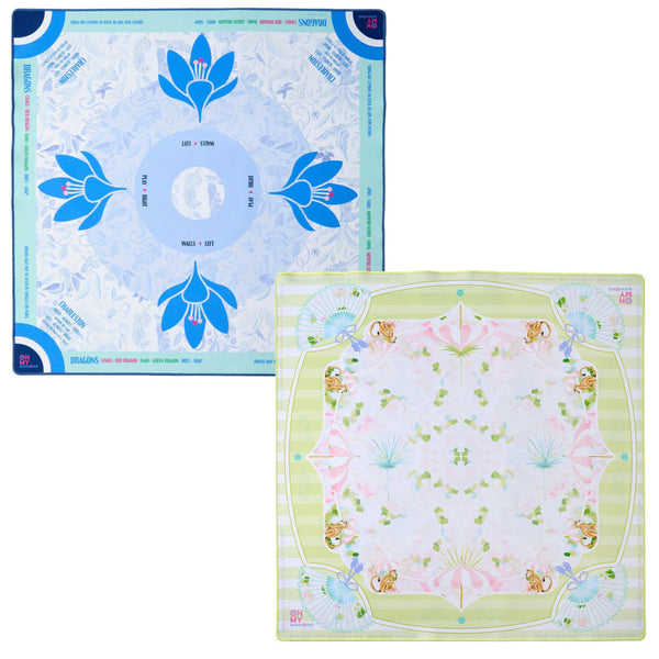 The Oh My Mahjong Mat Collection by Oh My Mahjong features two square scarves, reminiscent of elegant Mahjong mats. The left displays a blue floral design while the right combines light green and pink with floral and leaf motifs, both enhanced with a non-slip surface for enduring elegance.