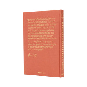The hardcover book "Malhadinha, The Soul of Alentejo" by Assouline stands upright, featuring a rust-colored textured cover with a printed quote and the author’s white signature—an ideal keepsake for lovers of Alentejo’s wine culture.