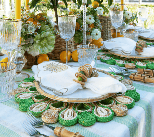 A table set for a meal with Kim Seybert's Marisol Placemat Collection, napkins with decorative rings, crystal glasses, and floral arrangements of lemons and white flowers.