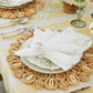 A table setting features a woven placemat, white plates, the Kim Seybert Bloom White Napkin Set with a floral napkin ring, and silver utensils atop a striped tablecloth.