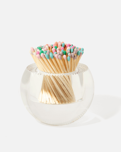 The Acrylic Match Striker Collection by Tart by Taylor features a clear round glass container filled with wooden matches tipped in pastel colors—a stylish, functional accessory perfect for your coffee table.